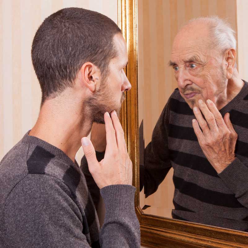 man looking into a mirror and thiking he sees an older man than he is, to illustrate how hormone imbalance can affect males